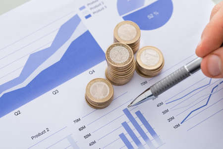 Cropped image of pen with line and coins graphs on desk