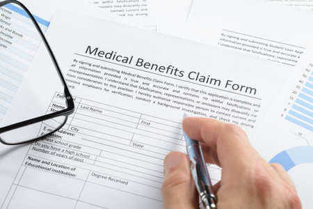 Close-up Of Hand Holding Pen Over Medical Claim Application Form