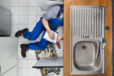 Male Plumber Examining Sink In Kitchen Holding Clipboardの写真素材