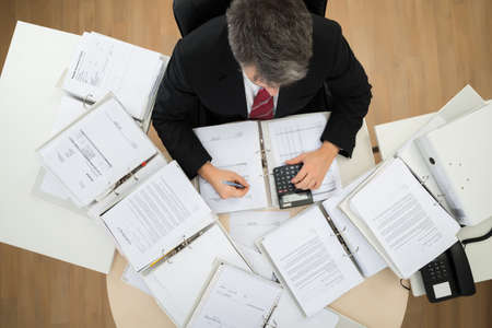 High Angle View Of Businessman Calculating Invoices At Office Deskの写真素材