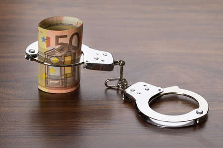 Close-up Of Euro Notes With Handcuffs On Wooden Tableの写真素材