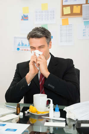 Mature Businessman At Office Desk Blowing His Noseの写真素材