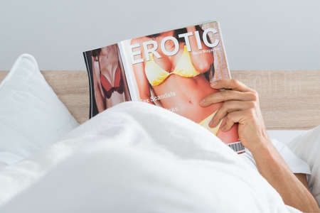 Close-up Of A Man Lying On Bed Reading Erotic Magazine At Homeの写真素材