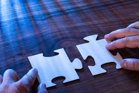 Close-up Of A Person Joining Two Jigsaw Pieces On Desk