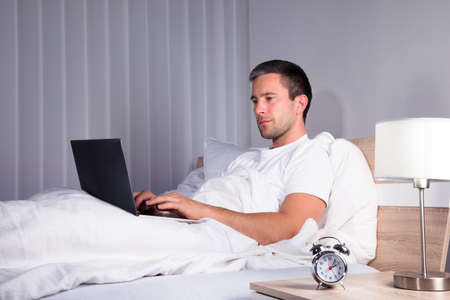 Man Using Laptop While Relaxing On Bedの写真素材