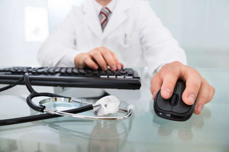 Doctor's Hand On Mouse And Keyboard In Front Of Stethoscopeの写真素材