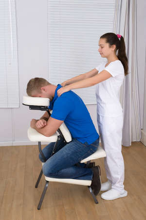 Female Physiotherapist Giving Shoulder Massage To Man On Massage Chairの写真素材
