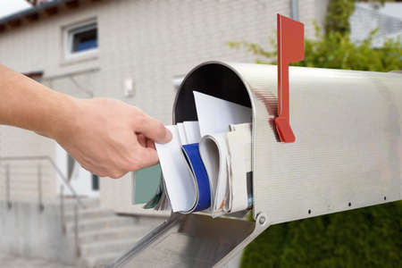 Close-up Of Man's Hand Taking Letter From Mailbox Outside Houseの写真素材