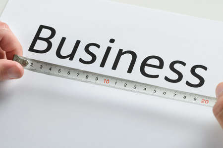 Close-up Of Person Hand Measuring The Text Business With Measure Tapeの写真素材