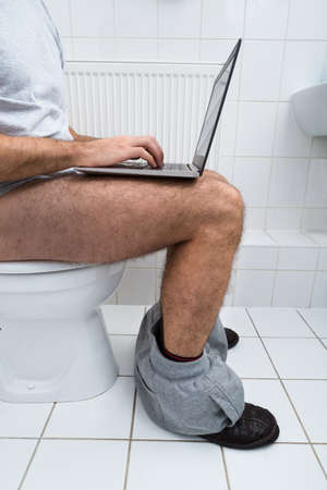 Close-up Of A Man Sitting On Commode Using Laptopの写真素材