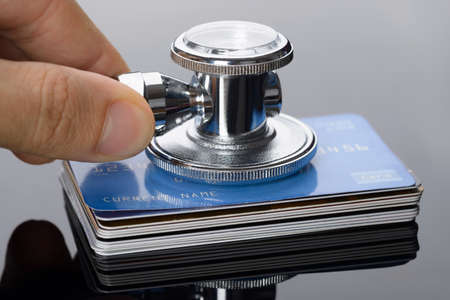 Close-up Of A Hand Holding Medical Stethoscope On Credit Card Stackの写真素材