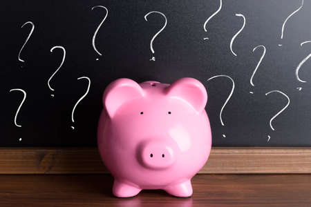 Piggy Bank In Front Of A Blackboard With Question Marksの写真素材