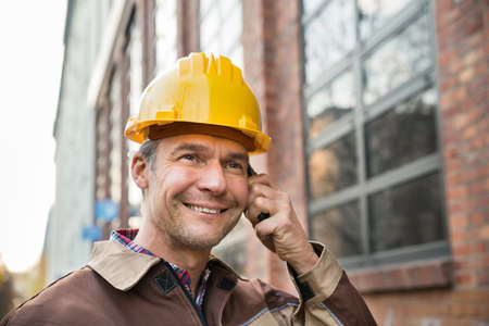 Close-up Of Happy Builder Wearing Hardhat Talking On Walkie Talkieの写真素材