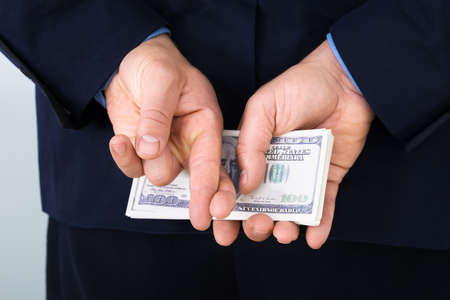 Businessman Standing With Crossed Finger And Holding Banknotes Behind His Backの写真素材
