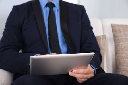 Close-up Of A Businessman Sitting On Couch Using Digital Tabletの写真素材