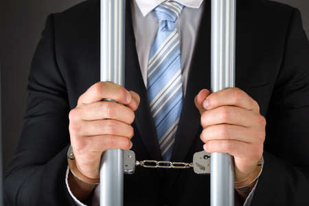 Close-up Of Handcuffed Businessman In Jail Holding Metal Barsの写真素材