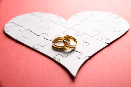 Golden Rings On Heart Made Of Puzzle Over Orange Backgroundの写真素材