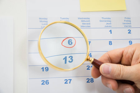 Close-up Of Person's Hand Holding Magnifying Glass Over Highlighted Dateの写真素材