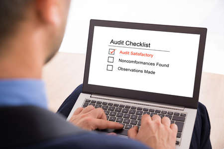 Close-up Of A Businessman Filling Audit Checklist Form On Laptopの写真素材