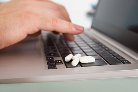 Close-up Of Person's Hand Using Laptop With Pills Over Keypadの写真素材