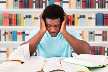 Worried African Student Looking At Books On Desk In Library