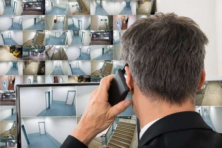Security System Operator Looking At Cctv Footage While Talking On Telephoneの写真素材