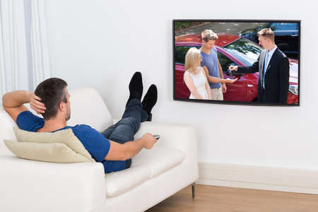 Rear View Of A Man Lying On Couch Watching Television