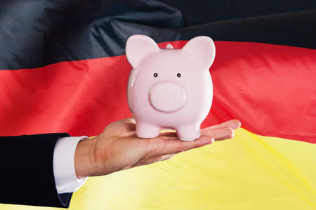 Businessman Holding Piggybank In Front Of German Flag