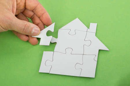 Close-up Of A Person's Hand Solving House Jigsaw Puzzleの写真素材