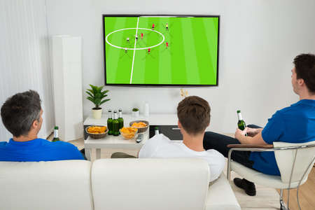 Three Men Sitting On Couch Watching Football Match On Television Three Men Sitting On Couch Watching Football Match On Television