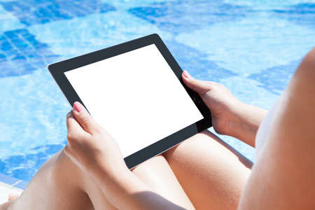 Midsection of young woman holding digital tablet with blank screen at poolsideの写真素材