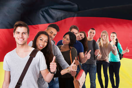 Group Of Multi Ethnic Students Standing In Front Of German Flag Showing Thumb Up