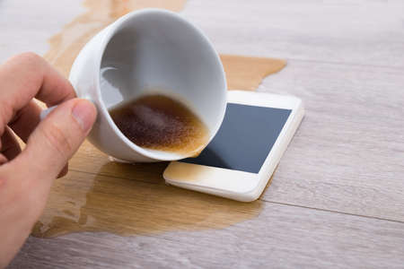 Close-up Of A Person's Hand Spilling Coffee On Cellphoneの写真素材