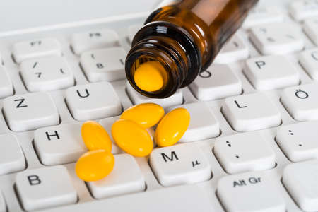 Close-up Of Pills Spilled From Bottle On Computer Keyboardの写真素材