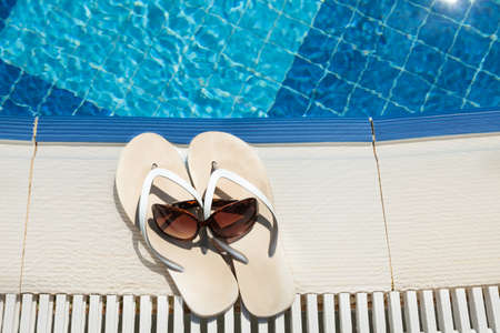 High angle view of flip flops and sunglasses beside swimming poolの写真素材