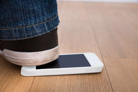 Close-up Of A Person's Foot Over Cellphone On Hardwood Floorの写真素材