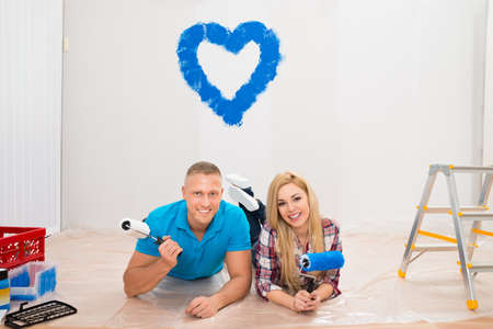 Portrait Of Young Couple With Paint Roller Lying On Floor In New Homeの写真素材