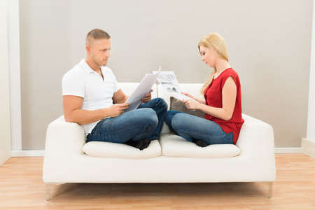 Young Couple Sitting On Sofa Reading Newspapers
