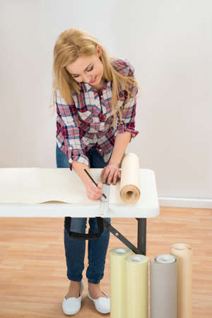 Portrait Of Young Woman Taking Measurement Of Wallpaper In New Home