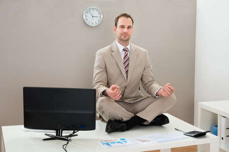 Businessman Doing Yoga On Desk In Officeの写真素材