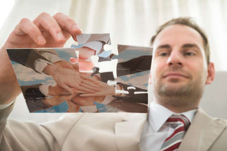 Low Angle View Of Businessman Inserting Last Puzzle Piece At Desk