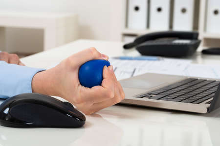 Close-up Of Businesswoman Hand Over Laptop Squeezing Stressballの写真素材