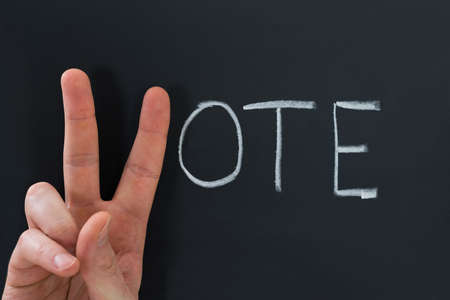 Close-up Of Finger Making V Sign With The Word Vote On Chalkboard