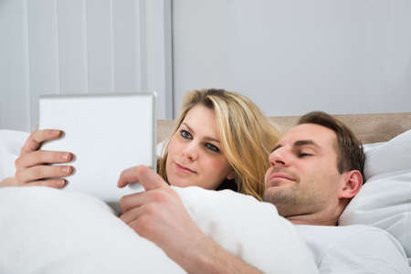 Happy Couple Using Digital Tablet In Bed At Homeの写真素材