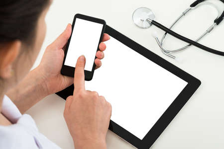 Close-up Of Doctor Using Blank Display Mobile Phone With Digital Tablet At Desk