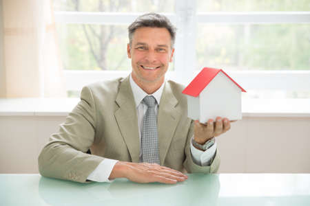 Portrait Of A Happy Businessman Holding House Model In Officeの写真素材