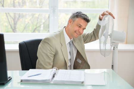 Portrait Of A Happy Businessman Sitting Near Fan In Officeの写真素材