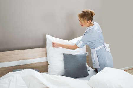 Female Housekeeping Worker Putting White Pillows In Bedroomの写真素材