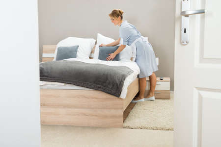Young Beautiful Maid Arranging Pillow On Bed In Hotel Room