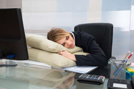 Young Businesswoman Sleeping On Pillow At Desk In Officeの写真素材